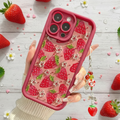 Phone case with strawberry pattern held by a hand on a light wooden background with strawberries and flowers.