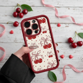 Phone case with cherry design held by a hand on a wooden surface with cherries and ribbons.