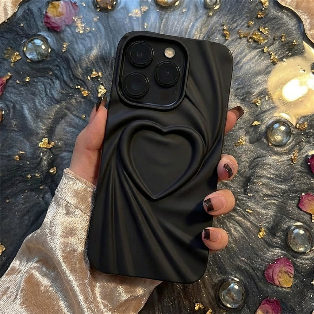 Black phone case with heart design held by a hand on a decorative surface