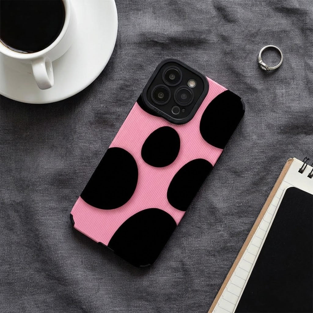 Pink phone case with black polka dots on a gray surface with a cup of coffee and notebook.
